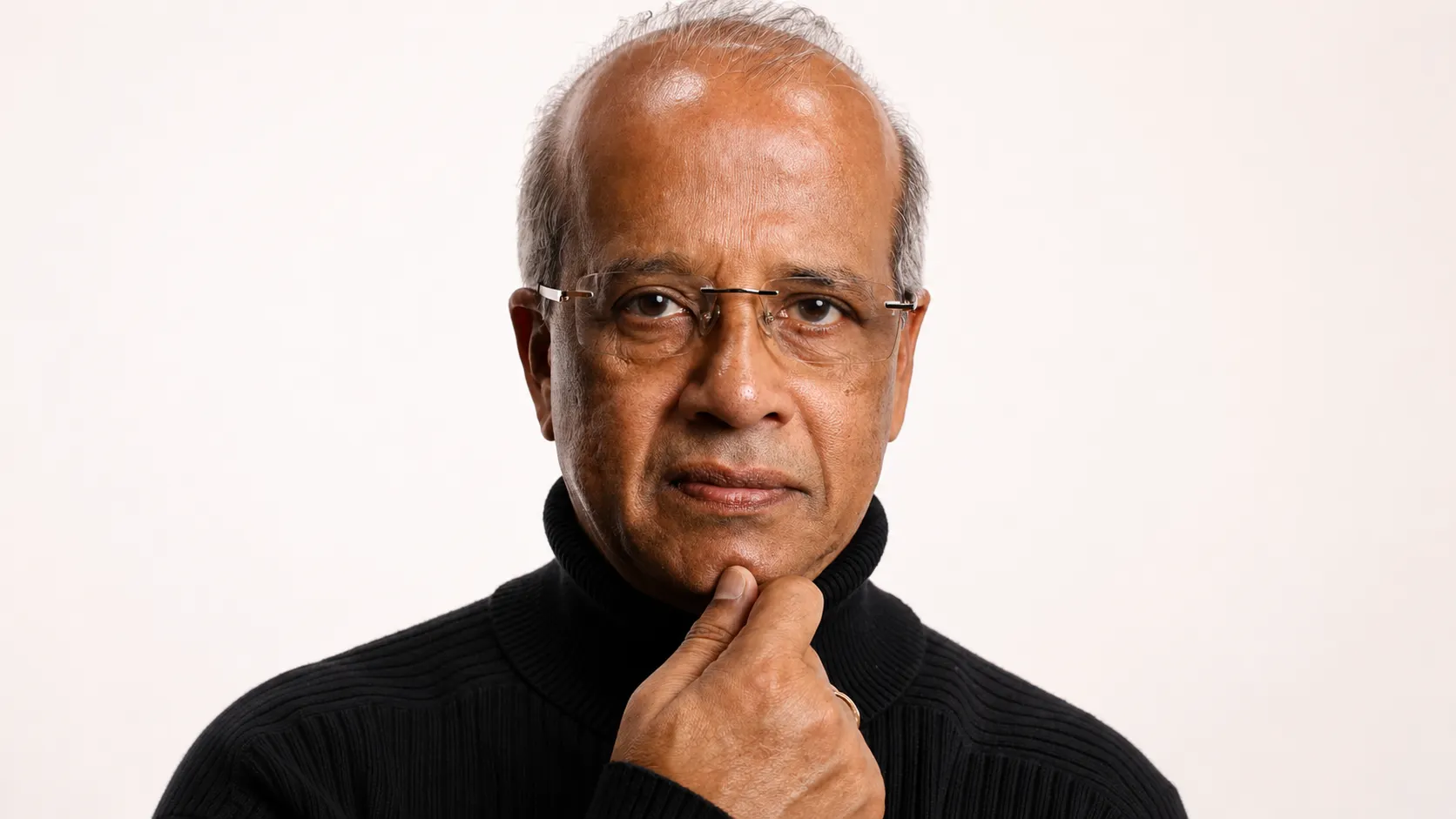 A stern retired man in rimless glasses and a black turtleneck